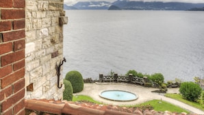 Blick aus einem Fenster auf einen See mit Bergen in der Ferne und einer Backsteinmauer links.