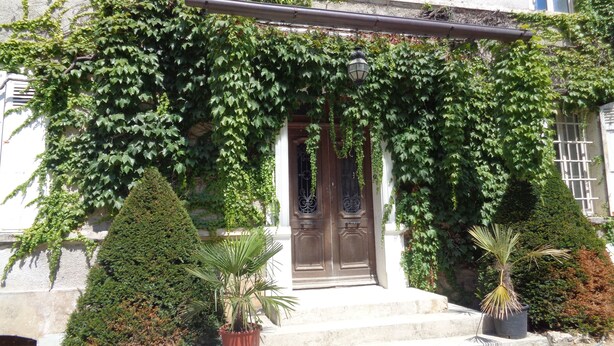 A building with a wooden door, steps, and a covered entrance with greenery. - L'annexe du Château de Saint Genix (Saint-Genix-les-Villages)