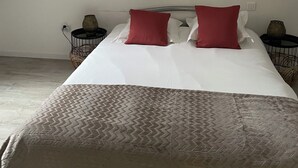 A bedroom with a sloped ceiling, a bed with white linens and two red pillows, and two nightstands with decorative items. - L'annexe du Château de Saint Genix (Saint-Genix-les-Villages)
