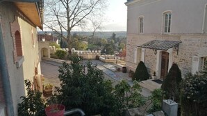 A courtyard with stone walls, potted plants, and a view of a distant landscape. - L'annexe du Château de Saint Genix (Saint-Genix-les-Villages)