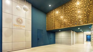 Un vestíbul d'hotel modern amb una paret blava, un panell decoratiu de fusta i un cartell que diu "GRAND'OR by CORDIA".