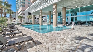 A pool area with lounge chairs and a modern building with large windows. - Crescent Keyes 810 | Oceanfront 3 Bedroom Condo (North Myrtle Beach)