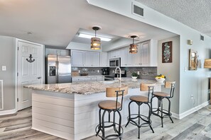 Cozinha moderna com uma ilha grande, banquetas, eletrodomésticos de aço inoxidável e iluminação pendente.