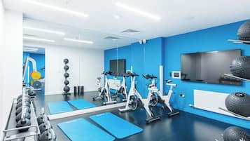 A modern gym with exercise bikes, weights, and a TV on the wall.