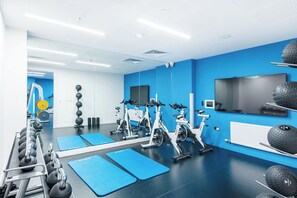 A modern gym with exercise bikes, weights, and a TV on the wall. - Yugo Kavanagh Court (Dublin)