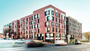 A modern multi-story building with a red brick facade and large windows.
