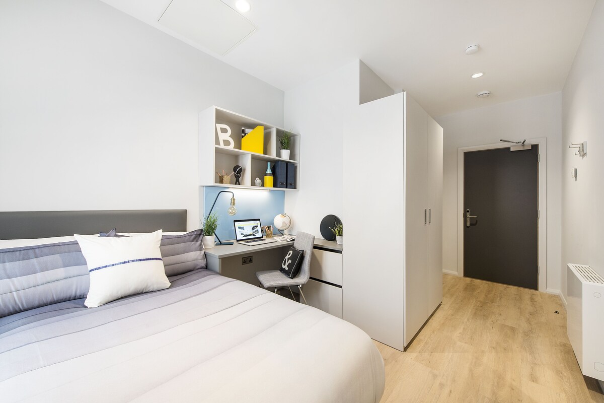 A modern bedroom with a bed, desk, chair, and built-in shelving.
