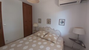 A bedroom with a bed, a wooden door, an air conditioner, and wall-mounted lamps.