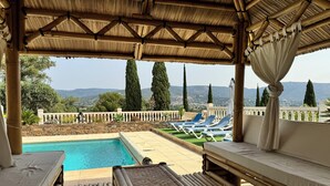 A poolside area with a bamboo pergola, lounge chairs, and a view of the landscape.