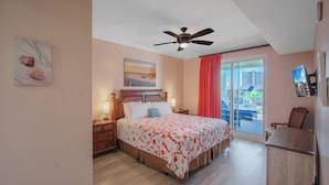Un dormitorio con cama, mesitas de noche, ventilador de techo, ventana con vistas y puerta que da a un balcón.