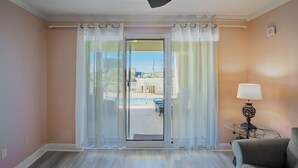 Una habitación con puerta corrediza de vidrio que da a una zona de piscina, ventilador de techo, lámpara de mesa y sofá.