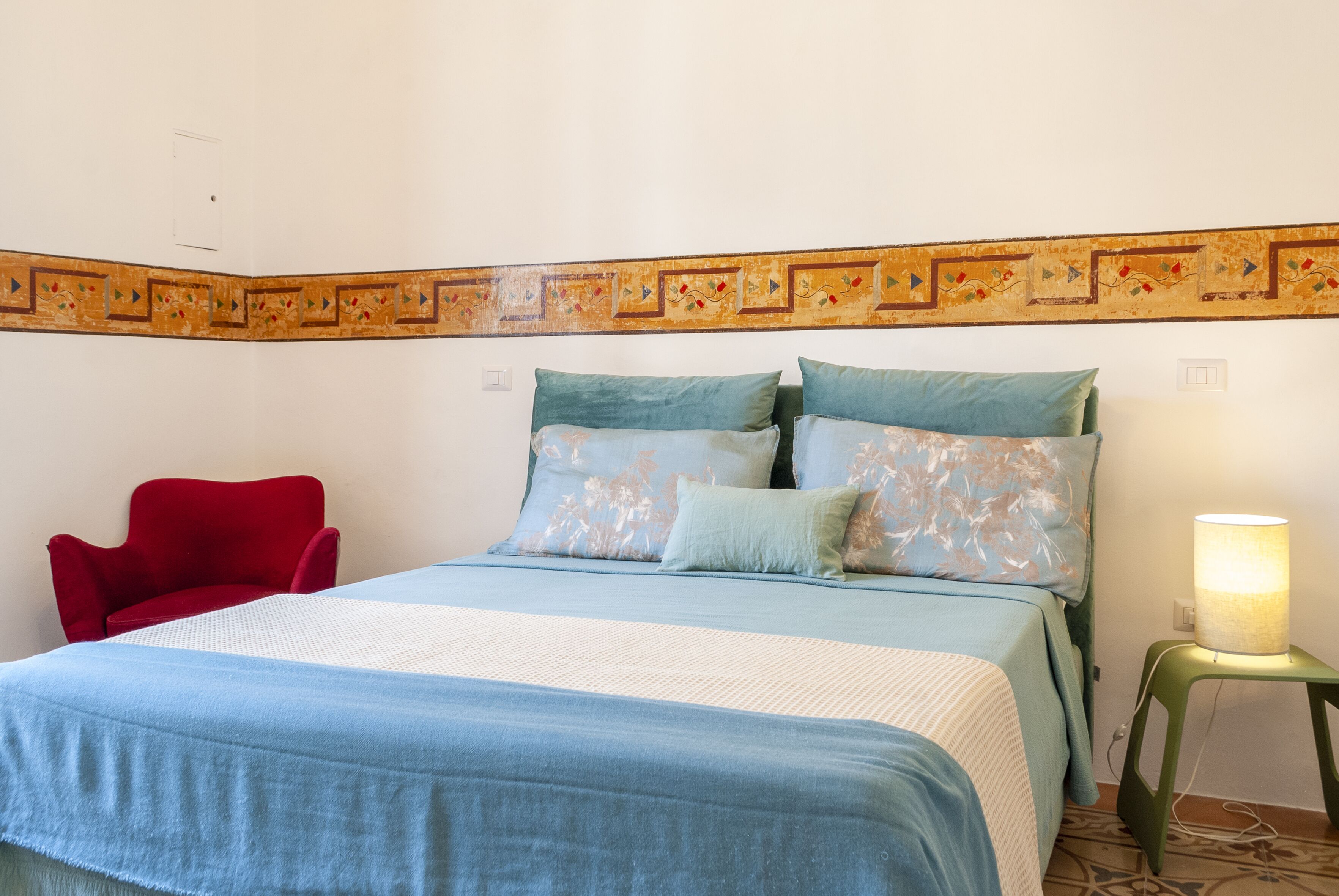 A bed with a blue and white bedspread, a red chair, and a small table with a lamp.