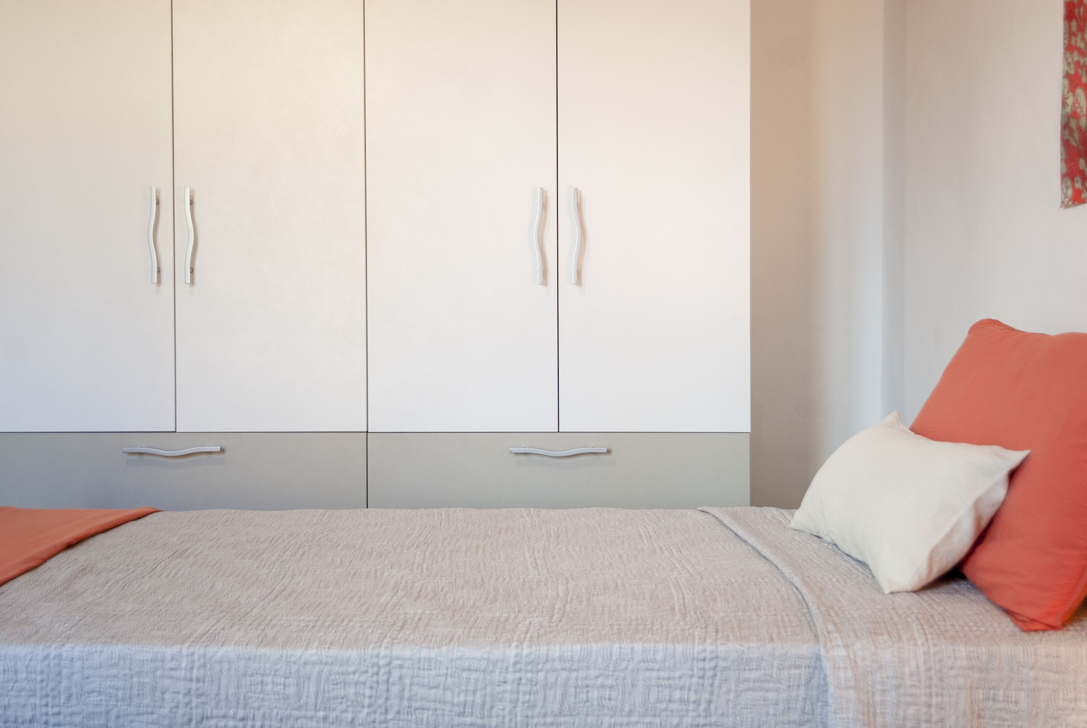 Quarto com uma cama, dois armários brancos e um travesseiro vermelho.