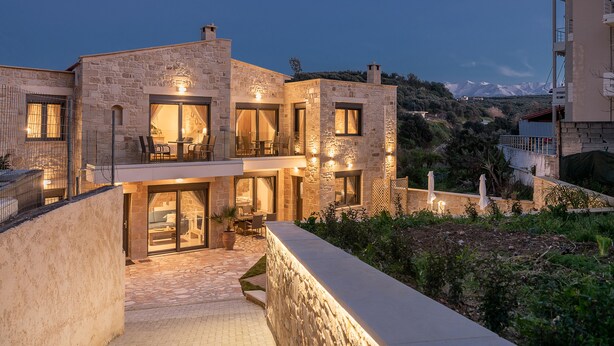 A stone building with a balcony and outdoor seating area, surrounded by greenery and a mountainous backdrop. - Villa Vanka (Chania)