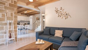 A modern living room with a blue sofa, wooden coffee table, and a stone wall. - Villa Vanka (Chania)