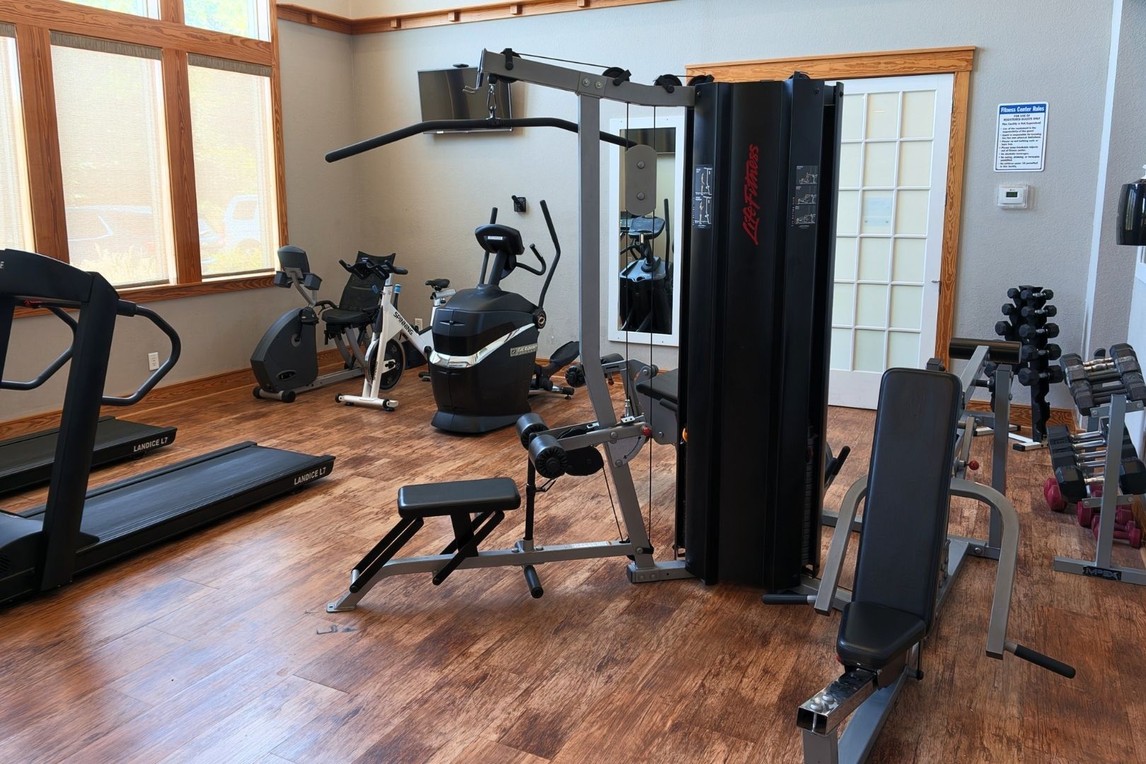 Een sportschool met diverse fitnessapparaten, waaronder loopbanden, een hometrainer en krachttoestellen.