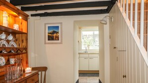 A wooden staircase leading to a kitchen with a window, a framed picture on the wall, and a shelf with dishes and a candle. - Bwthyn Dwyfor (Beaumaris)