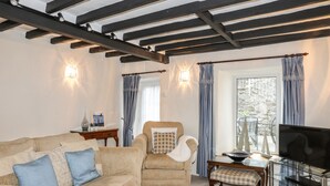 A living room with a sofa, armchair, and a TV on a glass table. - Bwthyn Dwyfor (Beaumaris)