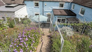 A blue house with a sloped roof, a small garden with purple flowers, and a metal fence. - Bwthyn Dwyfor (Beaumaris)
