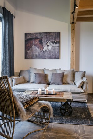 A living room with a sofa, a chair, a table with candles, and a painting of a horse. - Fantastic "Hochgern" vacation apartment on the Fasanenhöhe horse farm (Chieming)