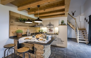 Eine moderne Küche mit Holzbalken, einer zentralen Kochinsel mit Barhocker und einer Treppe, die zu einem Schlafzimmerboden führt.
