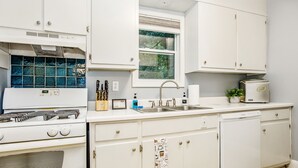 A kitchen with white cabinets, a stove, a sink, and a window. - The Woodside Guest House II (Fayetteville)