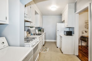 A compact kitchen with white cabinetry, a stove, microwave, and a sink. - The Woodside Guest House II (Fayetteville)