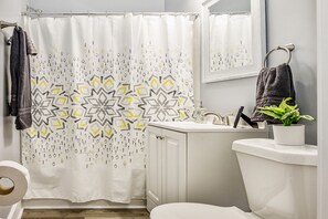 A bathroom with a shower curtain, a toilet, a sink, a mirror, and a towel rack.