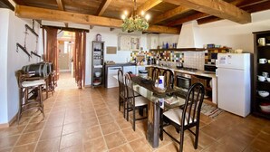 A rustic kitchen with wooden beams, a dining table with chairs, a washing machine, and a refrigerator. - Casa Tabobo - 2 bedroom rural house with breathtaking sea views and a hot tub. (Tías)