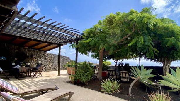 A covered outdoor seating area with a stone wall, wooden furniture, and potted plants. - Casa Tabobo - 2 bedroom rural house with breathtaking sea views and a hot tub. (Tías)