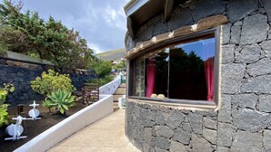 A stone building with a window and a small garden area with plants and a wooden bench. - Casa Tabobo - 2 bedroom rural house with breathtaking sea views and a hot tub. (Tías)
