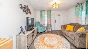 A living room with a television, a sofa, a chair, and a patterned rug. - The Cozy Cottage (Fayetteville)