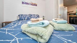 A neatly made bed with a blue and white patterned bedspread, a pillow, and a stack of folded towels in various colors. - The Cozy Cottage (Fayetteville)
