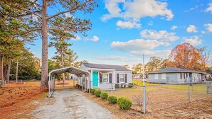 A single-story house with a covered porch, a fenced yard, and a clear sky. - The Cozy Cottage (Fayetteville)