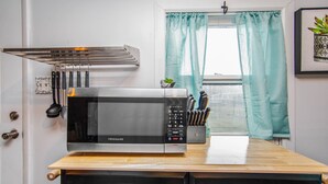 A kitchen with a Frigidaire microwave on a wooden countertop, a set of knives in a holder, and a window with teal curtains. - The Cozy Cottage (Fayetteville)
