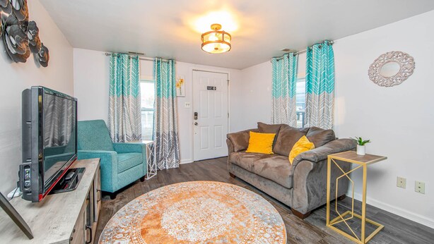 A living room with a sofa, a TV, a coffee table, and curtains. - The Cozy Cottage (Fayetteville)