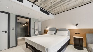 Una camera d'albergo moderna con un letto grande, comodini, uno specchio e una piccola area salotto.