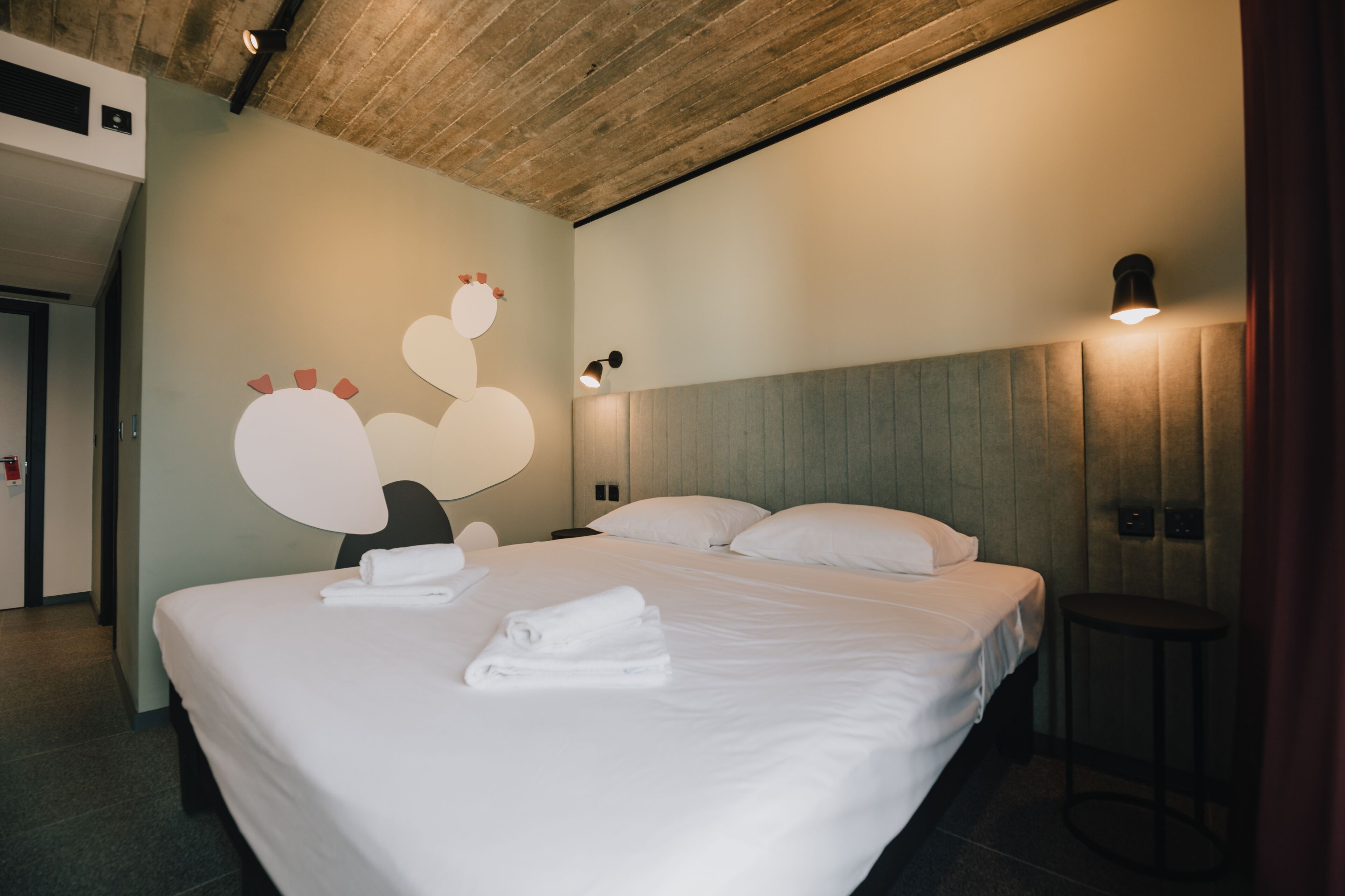 A hotel room with a large bed, a wooden ceiling, and a wall with a circular design.