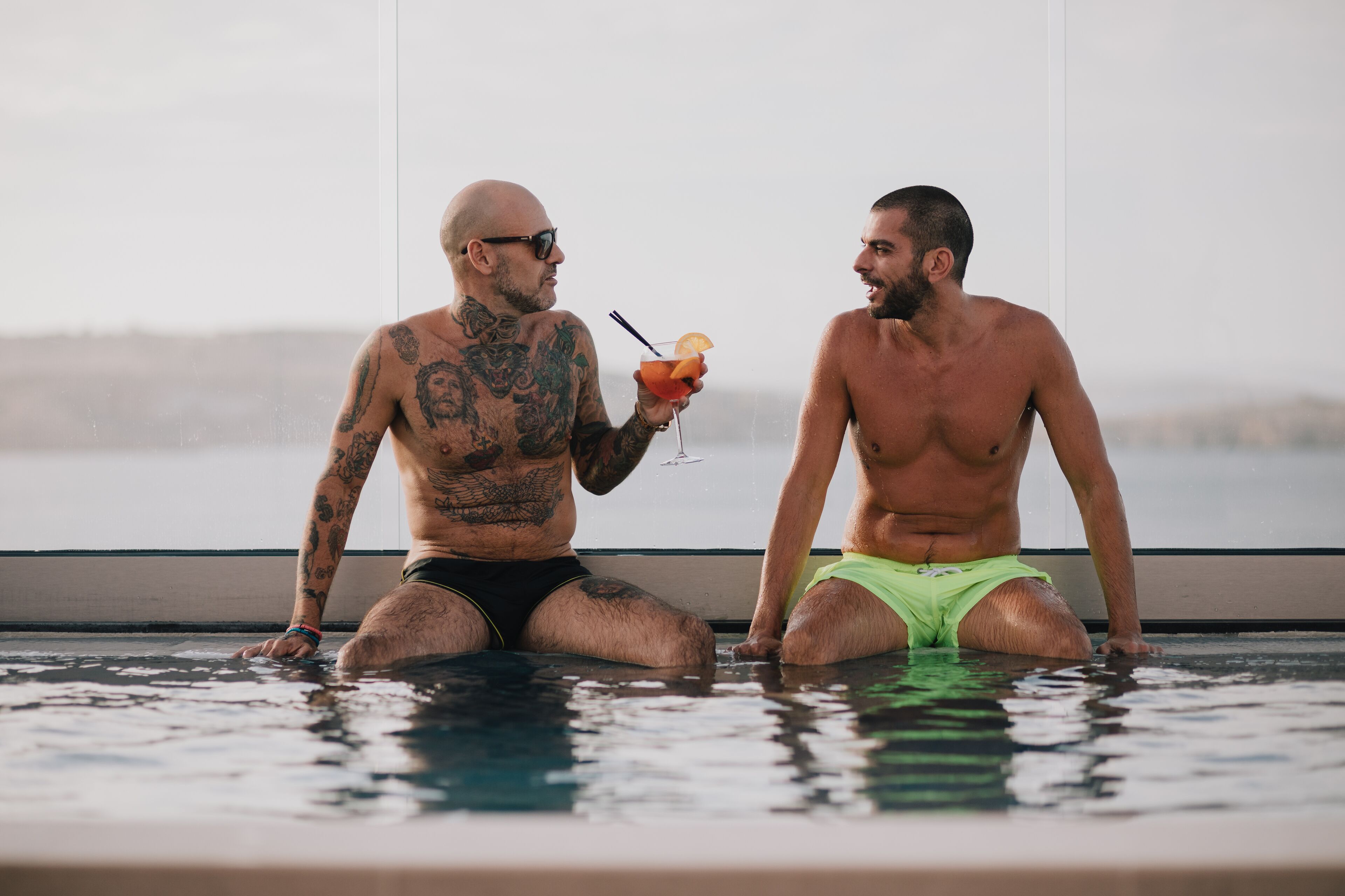Dos hombres sentados en una piscina con vista al mar.