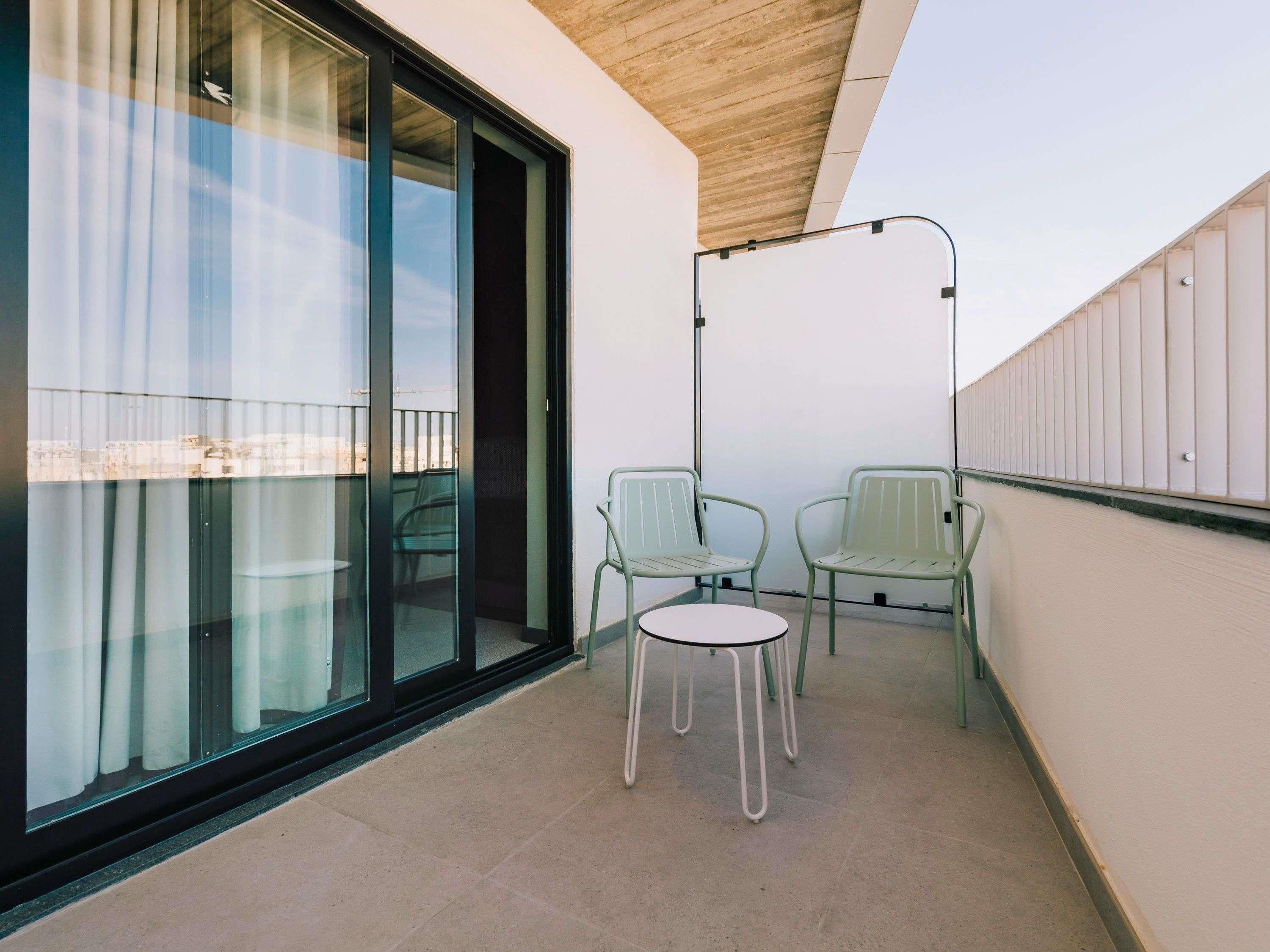 A balcony with two chairs and a table, a glass door, and a wooden ceiling.