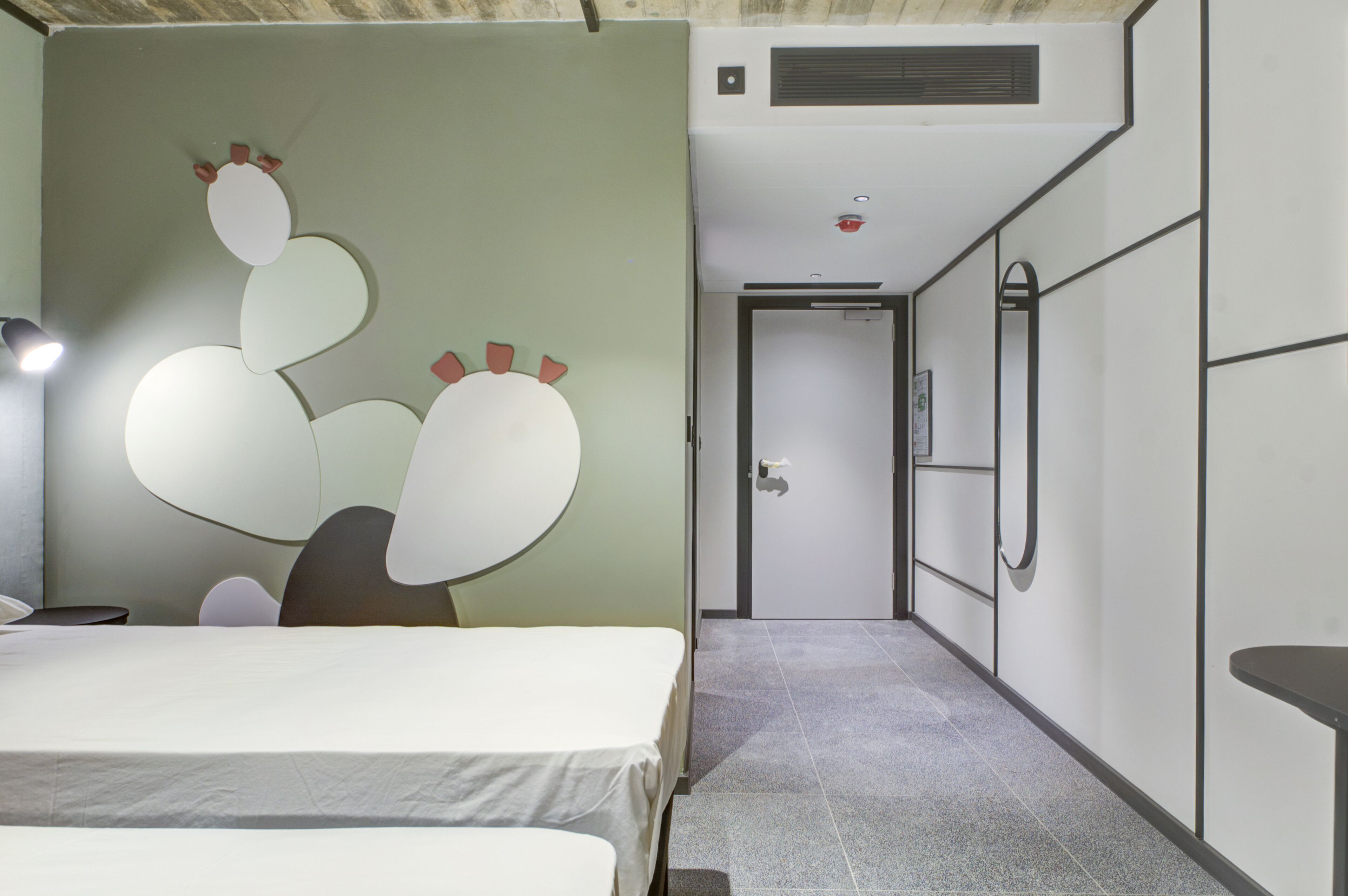 Une chambre d’hôtel avec un lit, un miroir fixé au mur et une porte donnant sur un couloir.