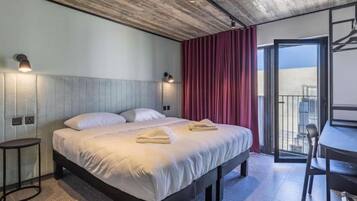 Habitación de hotel con cama, mesitas de noche, un escritorio y un balcón.