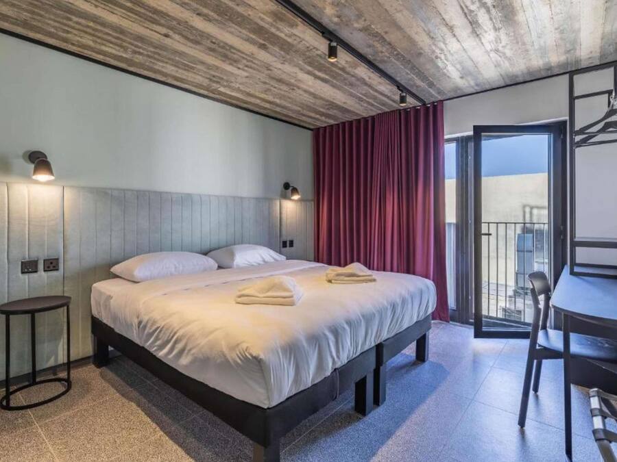 Quarto de hotel com cama, mesas de cabeceira, escrivaninha e varanda.