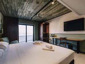A hotel room with a large bed, a desk, a chair, a television, and a balcony with a view. - Ibis Styles St. Paul's Bay Malta (St. Paul's Bay)