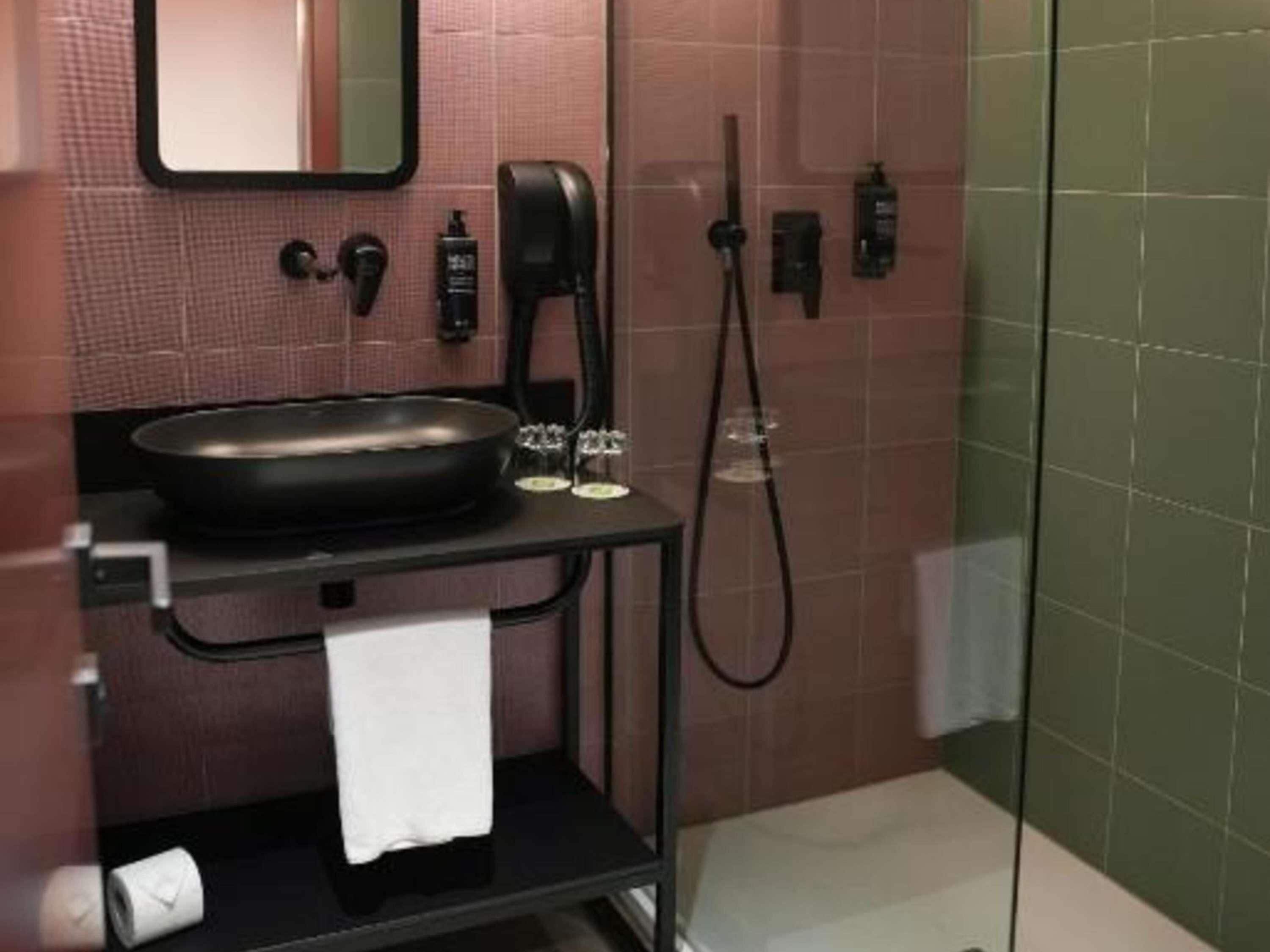 A bathroom with a black sink, a mirror, a towel rack, a handheld showerhead, and a glass-enclosed shower area.