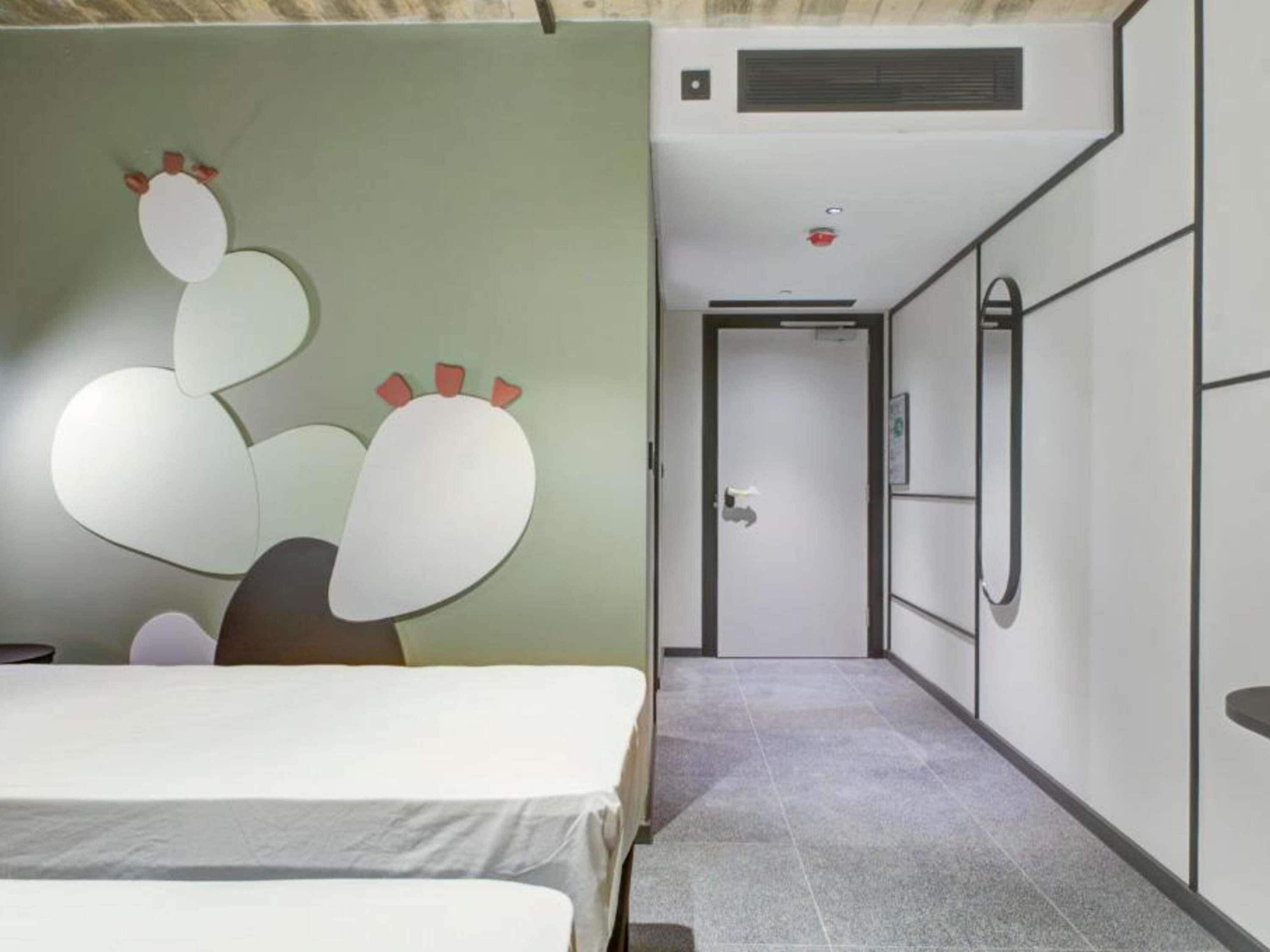 A hotel room with a bed, a wall-mounted artwork, a door, and a built-in air conditioning unit.