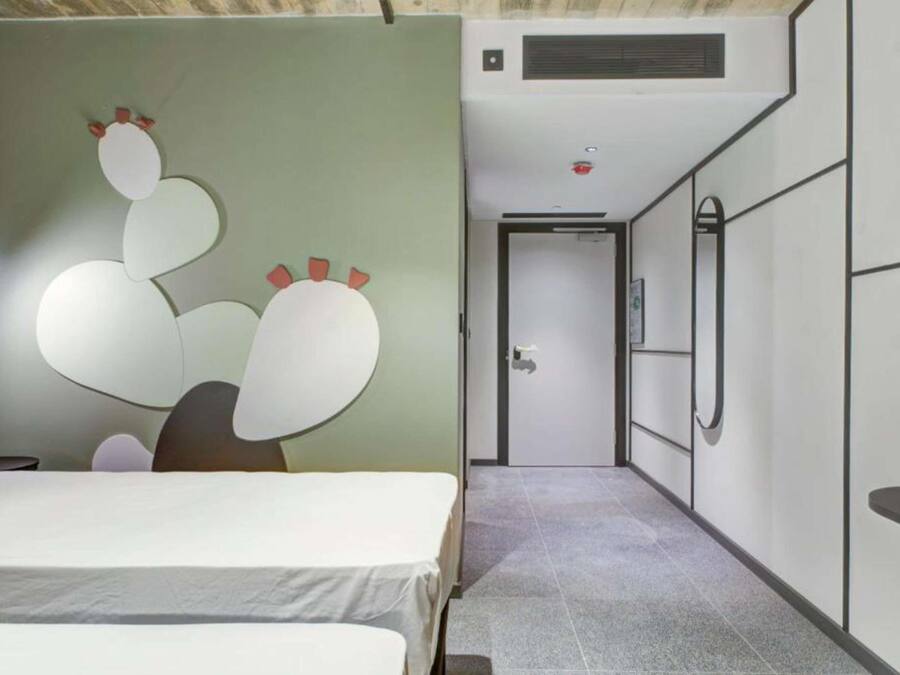 Quarto de hotel com uma cama, uma obra de arte na parede, uma porta e um ar condicionado embutido.