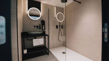 A modern bathroom with a black vanity, a round mirror, a handheld showerhead, and a glass-enclosed shower.
