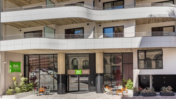 Un edificio a più piani con facciata curva, balconi e un negozio chiamato "Ibis Styles".