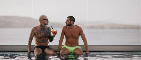 Two men sitting in a swimming pool with a view of the sea.
